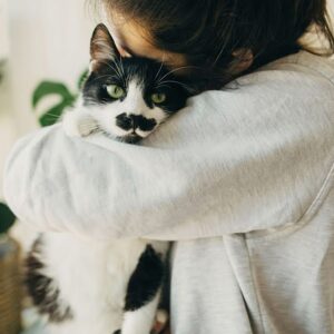 a woman hugging a black and white cat
