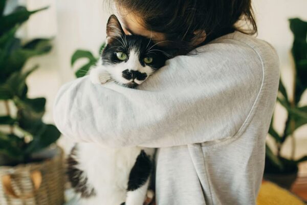 a woman hugging a black and white cat